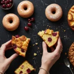 Assortment of sourdough desserts including cherry cakes, glazed donuts, and crumb cake on black marble surface