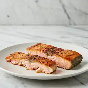 Crispy salmon belly pieces with golden-brown exterior and moist pink flesh on a white plate with marble background