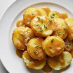 Golden Yukon potatoes smothered in rich savory gravy with fresh thyme sprigs on a white plate