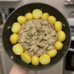 A skillet filled with golden baby potatoes arranged around a creamy stroganoff sauce, garnished with herbs.