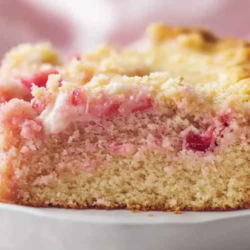 Fresh rhubarb stalks, eggs, flour, butter, and other baking ingredients arranged on a wooden surface