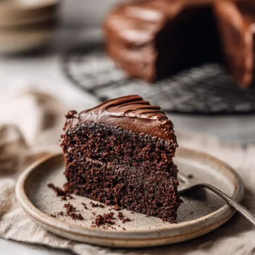 Chocolate cake slice on ceramic plate with soft frosting and crumbs
