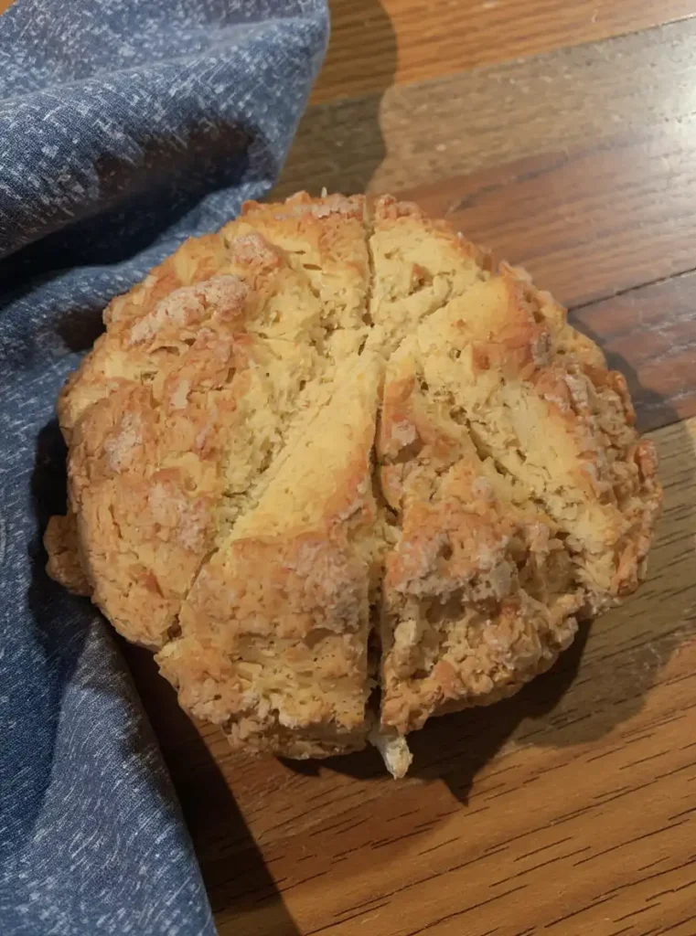 Golden-brown round sourdough Irish soda bread on wooden table
