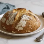Freshly baked gluten-free Irish soda bread on a white plate with butter and knife on marble background