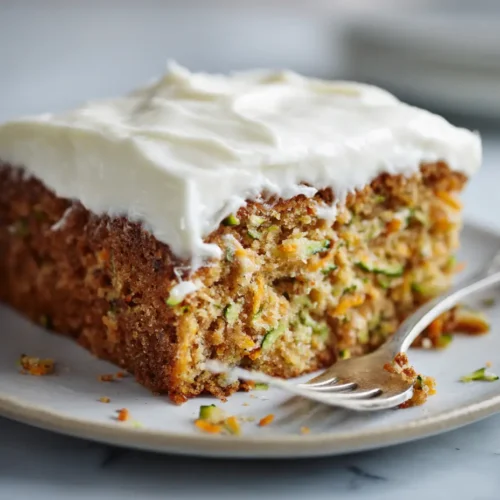 Moist zucchini squash cake slice with cream cheese frosting on a marble plate