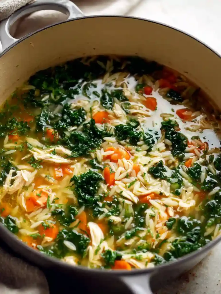 A partially overhead shot of lemon chicken orzo soup simmering in a Dutch oven