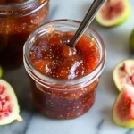 Homemade fig jam in a jar with fresh figs sliced around it