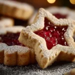 Shortbread Linzer cookies filled with raspberry jam on a white plate.