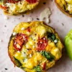 Baked egg muffins filled with vegetables and cheese in a muffin tin