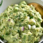 Herby avocado egg salad in a bowl, garnished with fresh herbs.